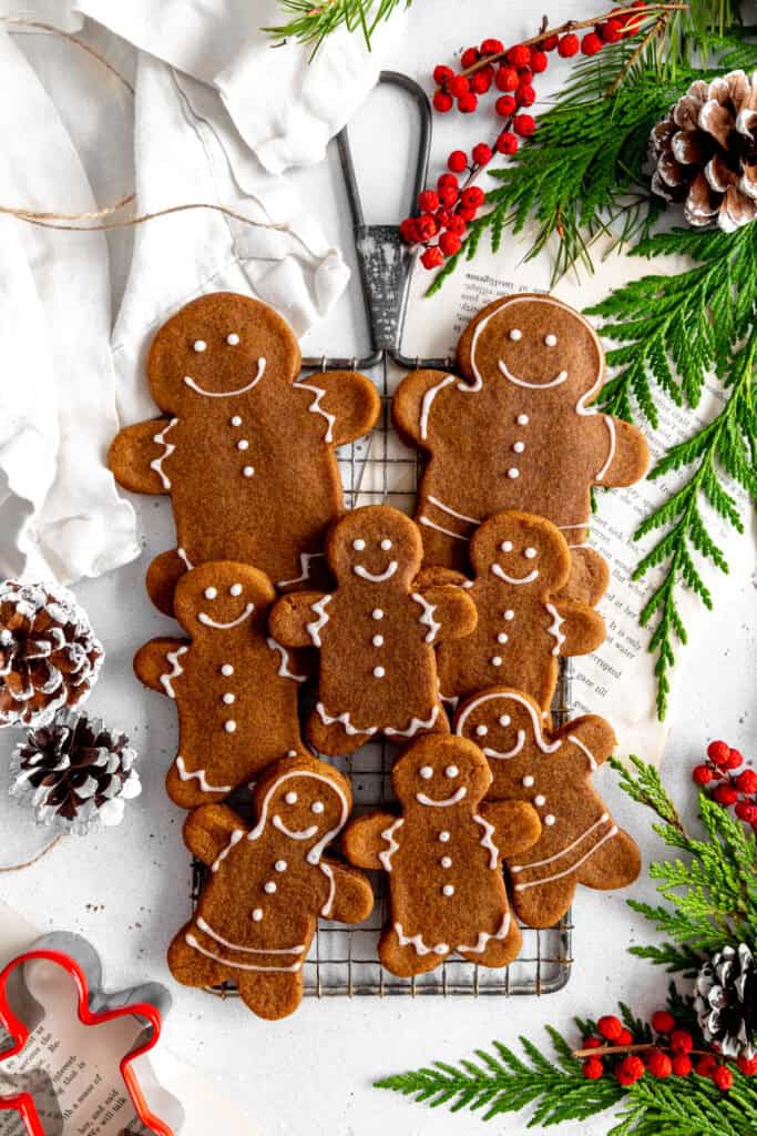 Gingerbread people on a wire cooling rack surrounded by pinecones and holly berries.