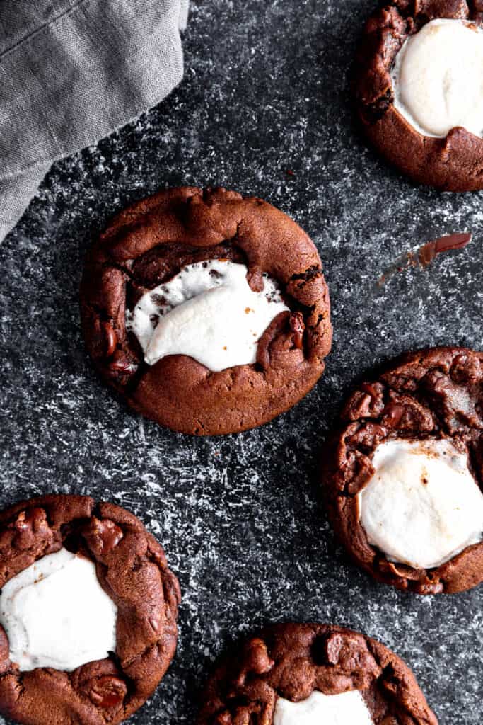 Hot chocolate cookies spread out on a dark surface.