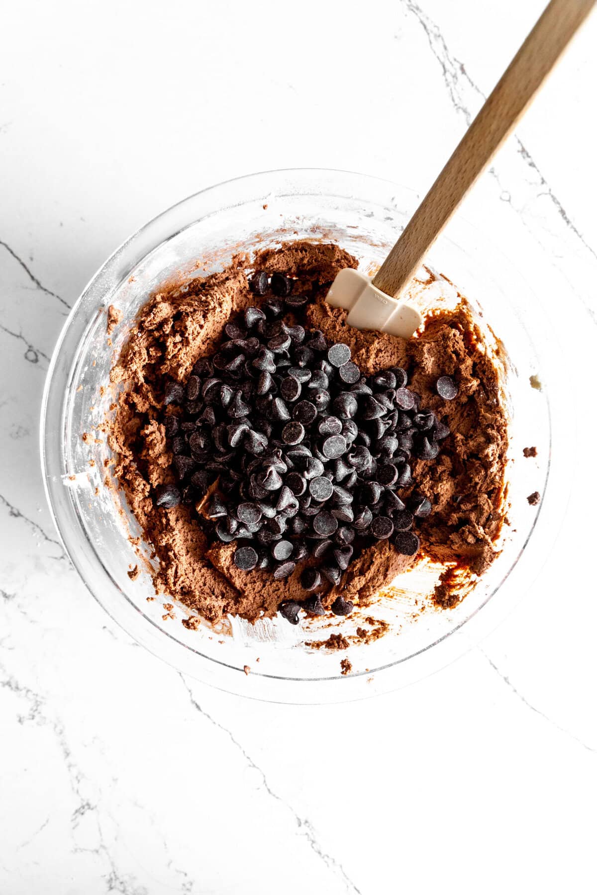 Glass bowl of chocolate cookie dough with a pile of chocolate chips on top.