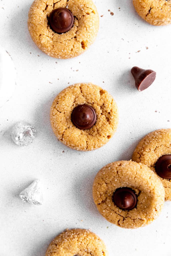 Peanut butter blossom cookies on a white background with more chocolate candies.