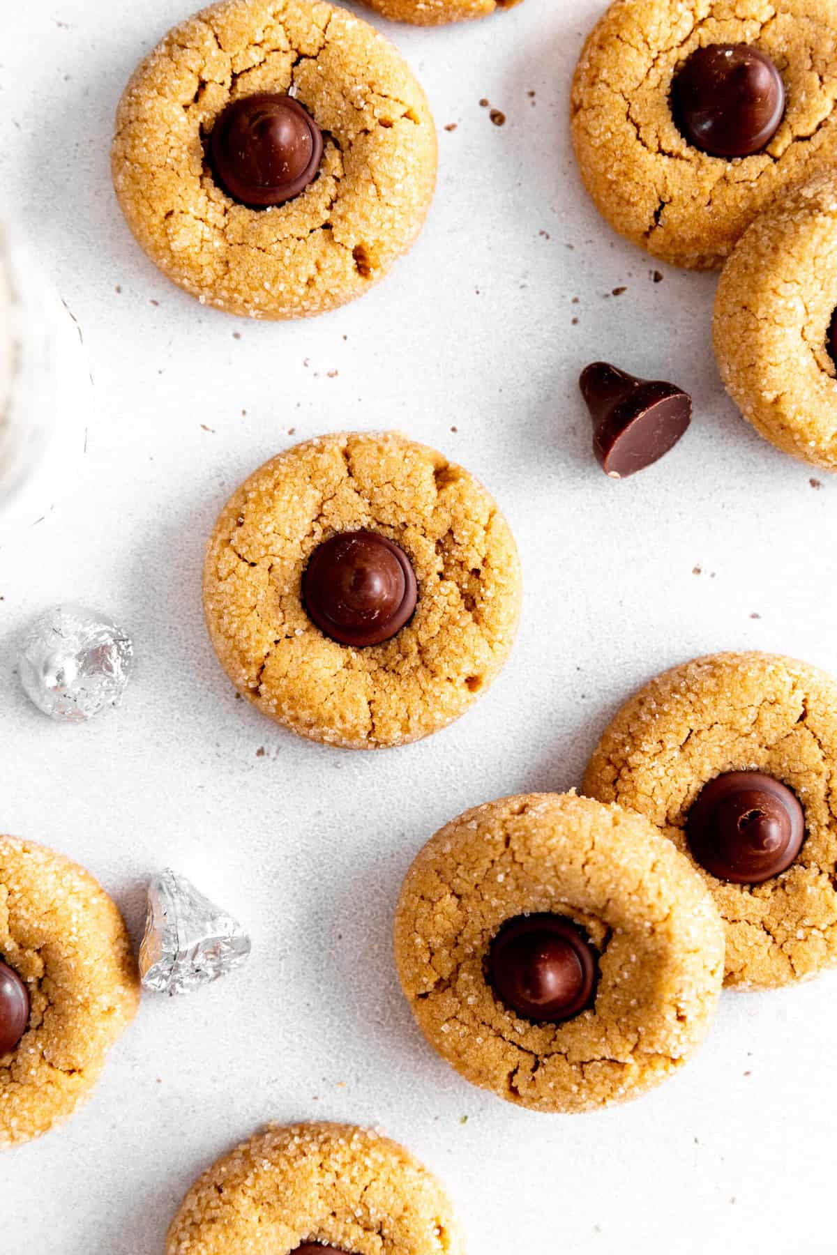 Peanut butter blossom cookies on a white background with more chocolate candies.