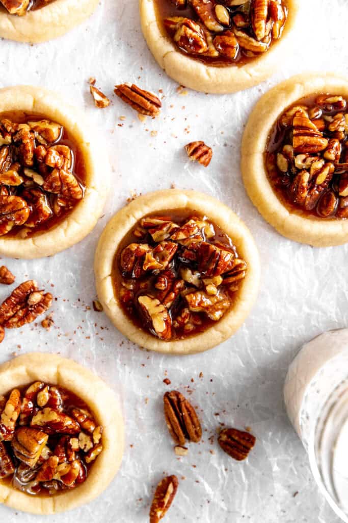 Vegan pecan pie cookies, a glass of milk and scattered pecans.