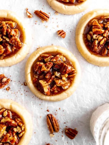 Vegan pecan pie cookies, a glass of milk and scattered pecans.