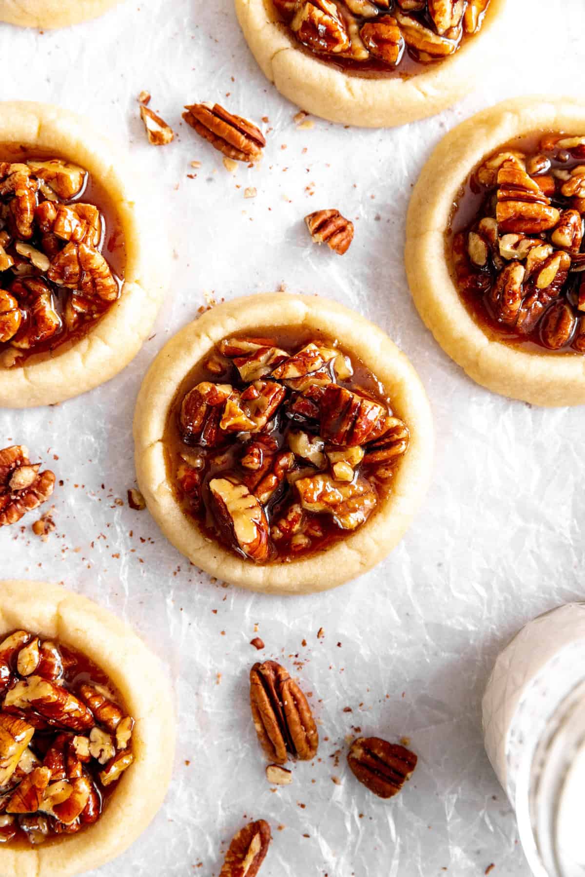 Vegan pecan pie cookies, a glass of milk and scattered pecans.