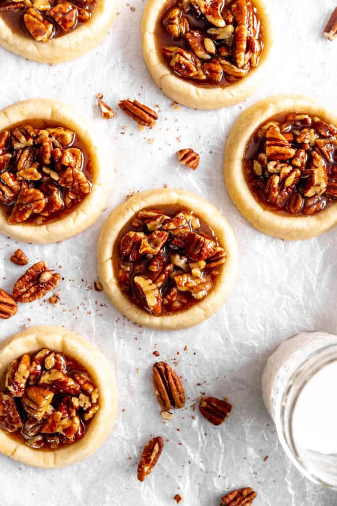 Vegan pecan pie cookies, a glass of milk and scattered pecans.