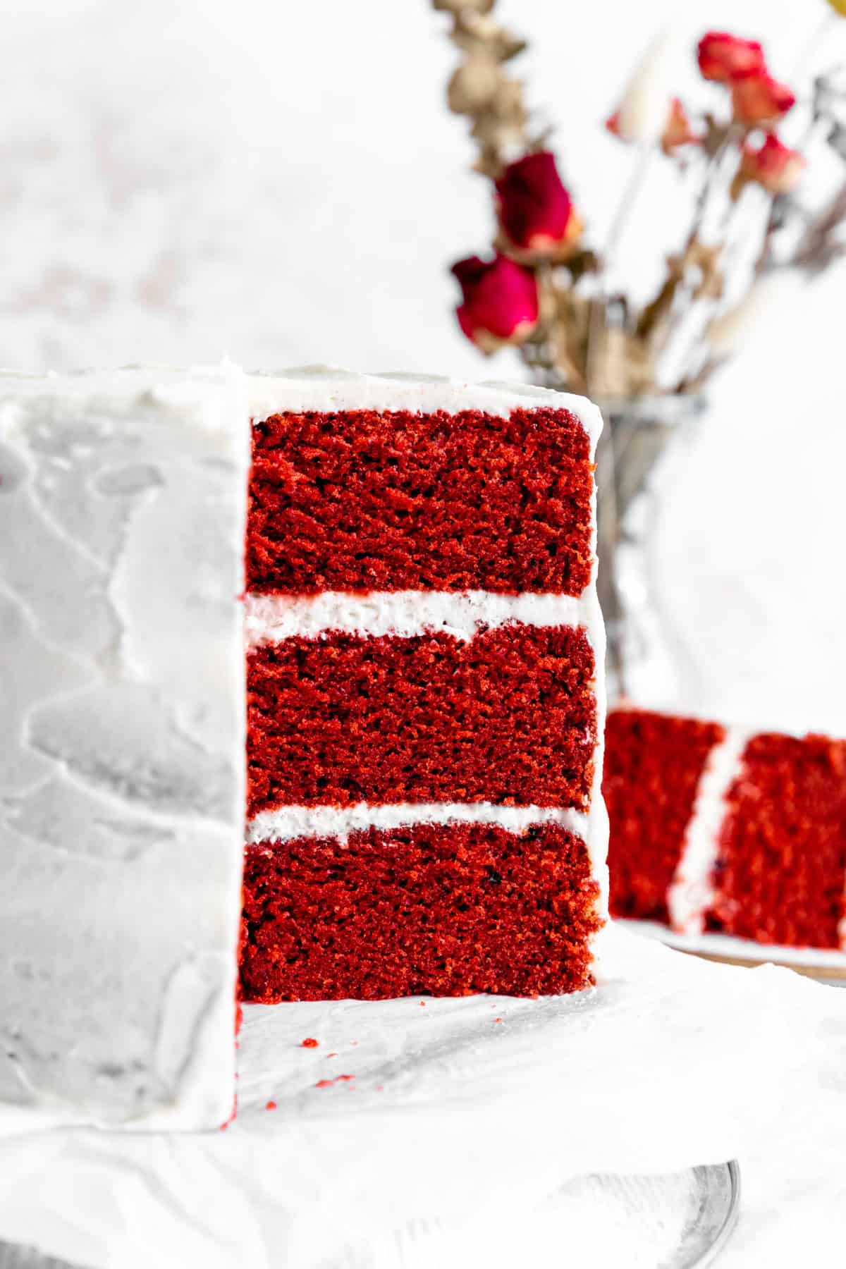 Red velvet cake in front of a vase of roses.