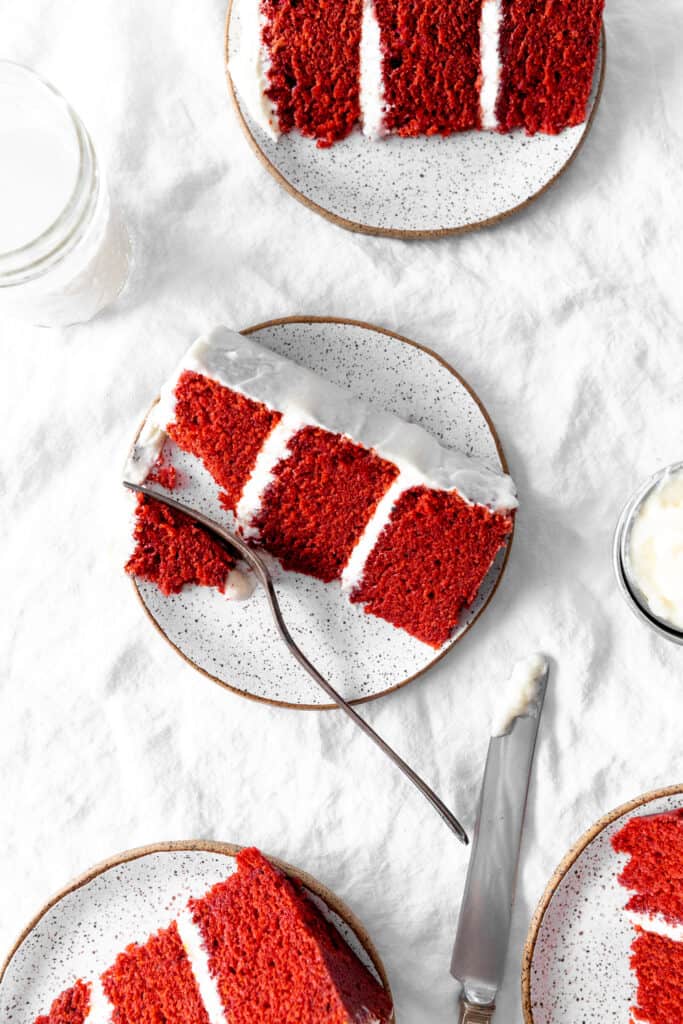 Four slices of red velvet cake on plates and a glass of milk.