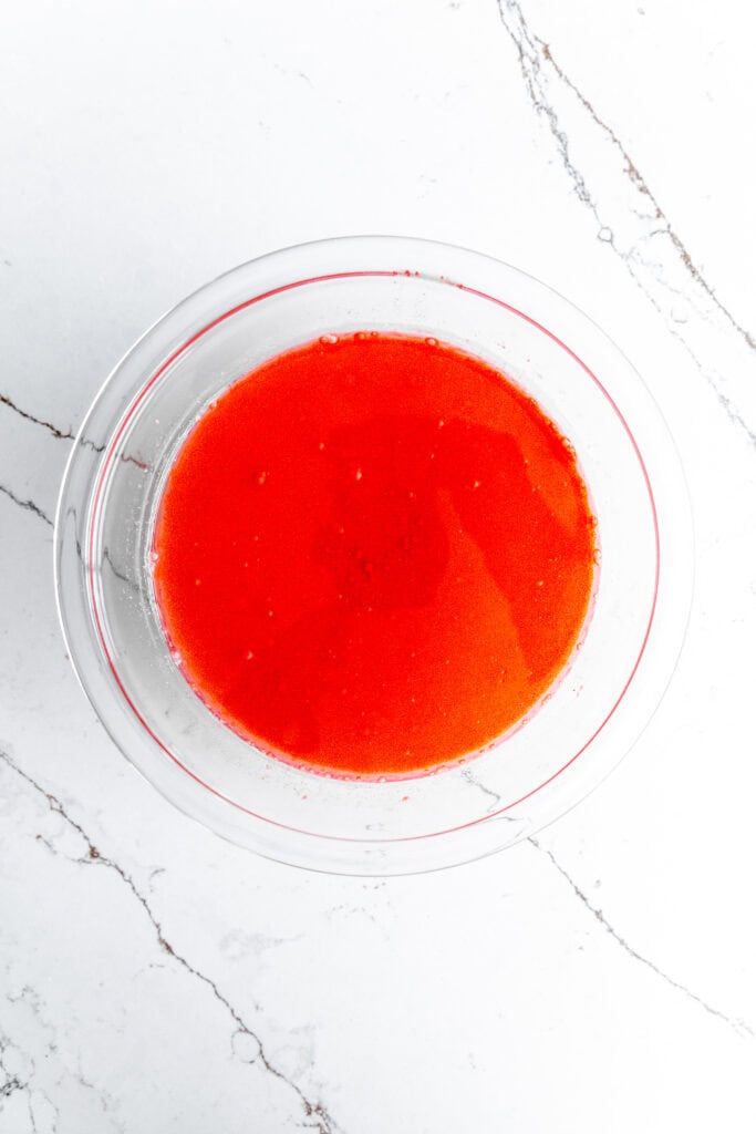 Glass bowl of mixed together milk, oil and red food coloring.