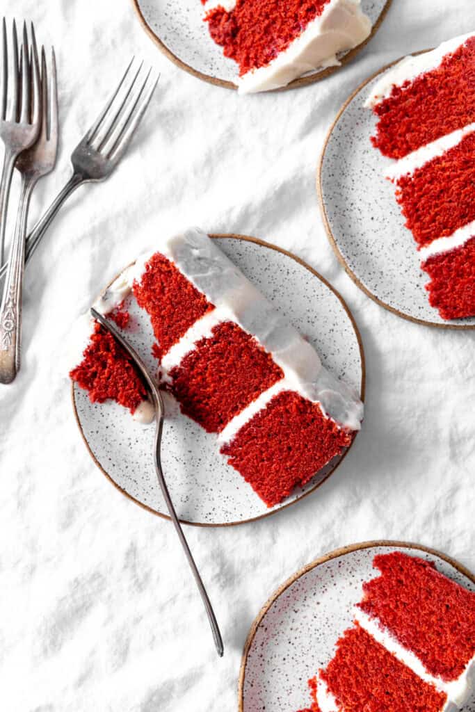 Four slices of red velvet cake on plates and a stack of silver forks.