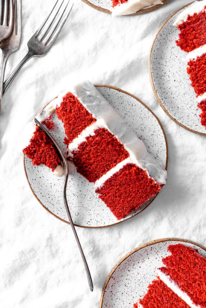 Fork cutting into a slice of red velvet cake surrounded by more sliced of cake on plates.