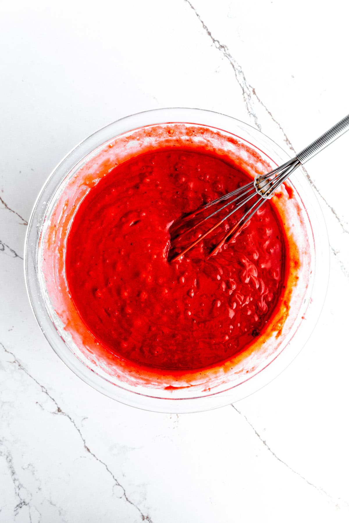 Glass bowl of red velvet cake batter and a whisk.