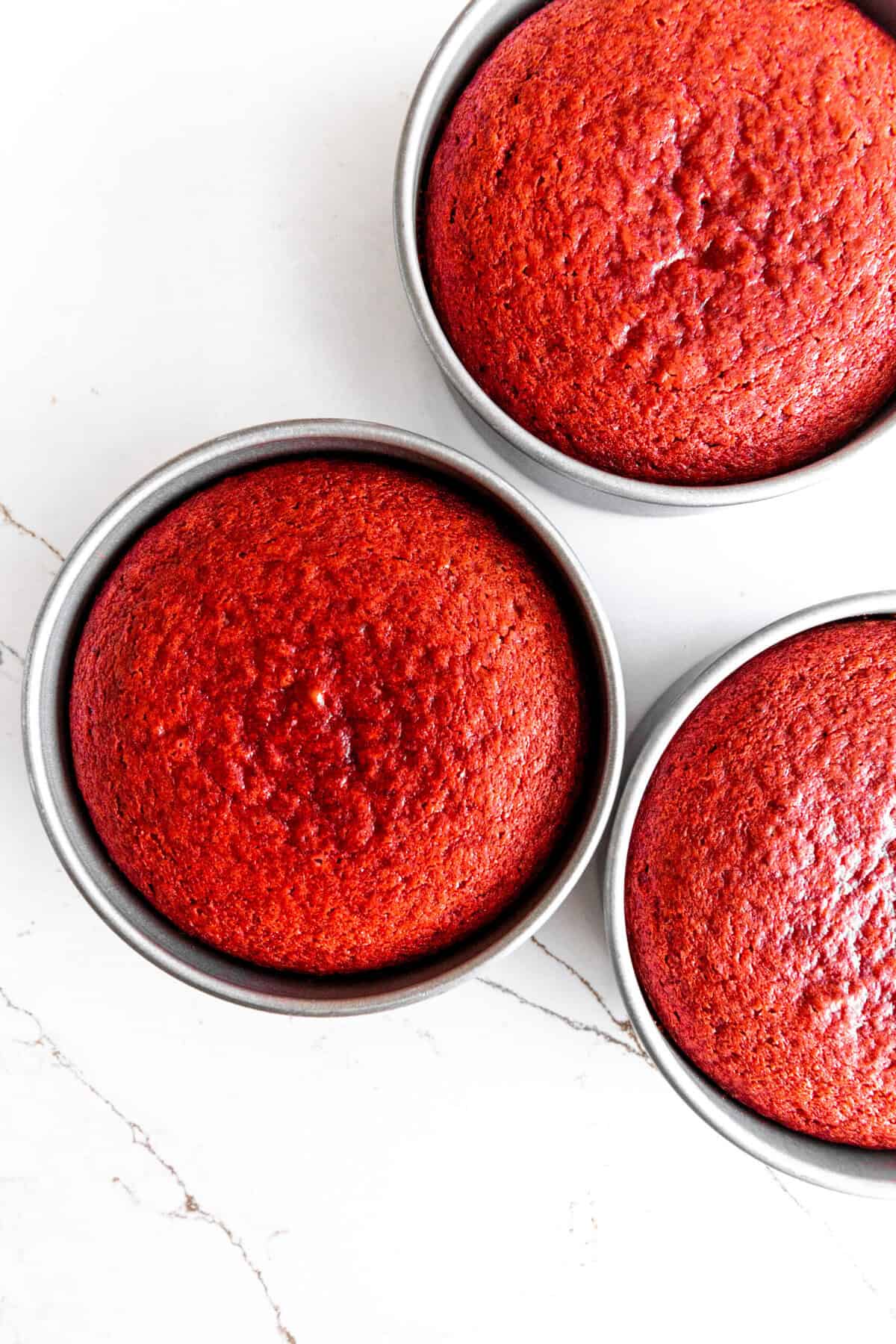 Baked red velvet cake layers in three round cake pans.