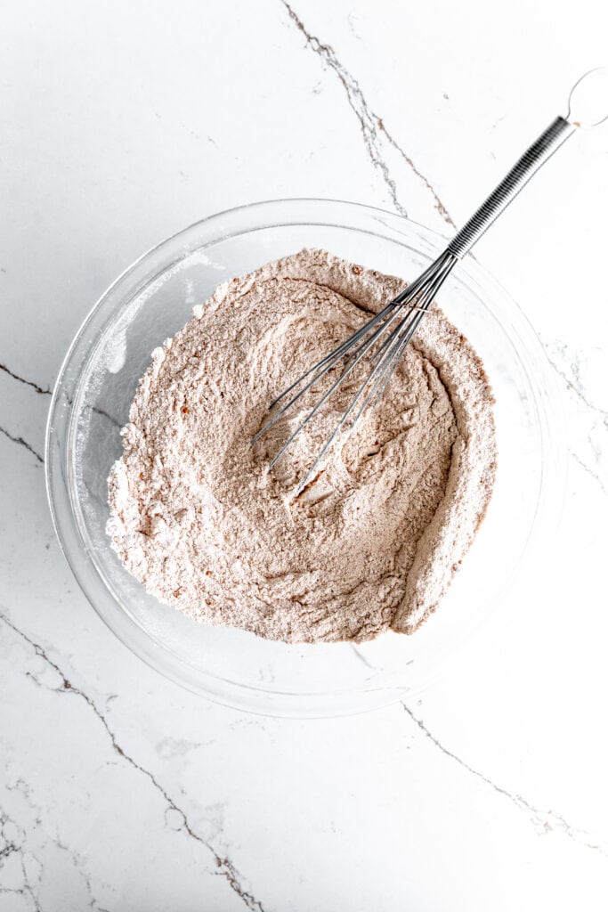 Glass bowl of flour, sugar, cocoa powder and a whisk.