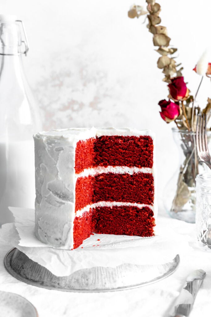 Red velvet cake, a jug of milk, a vase of roses and a cup of forks.