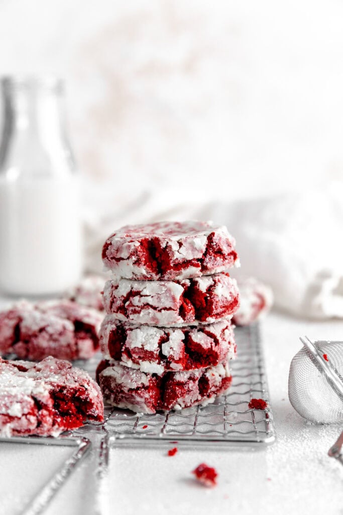 Stack of red velvet crinkle cookies and a jug of milk.