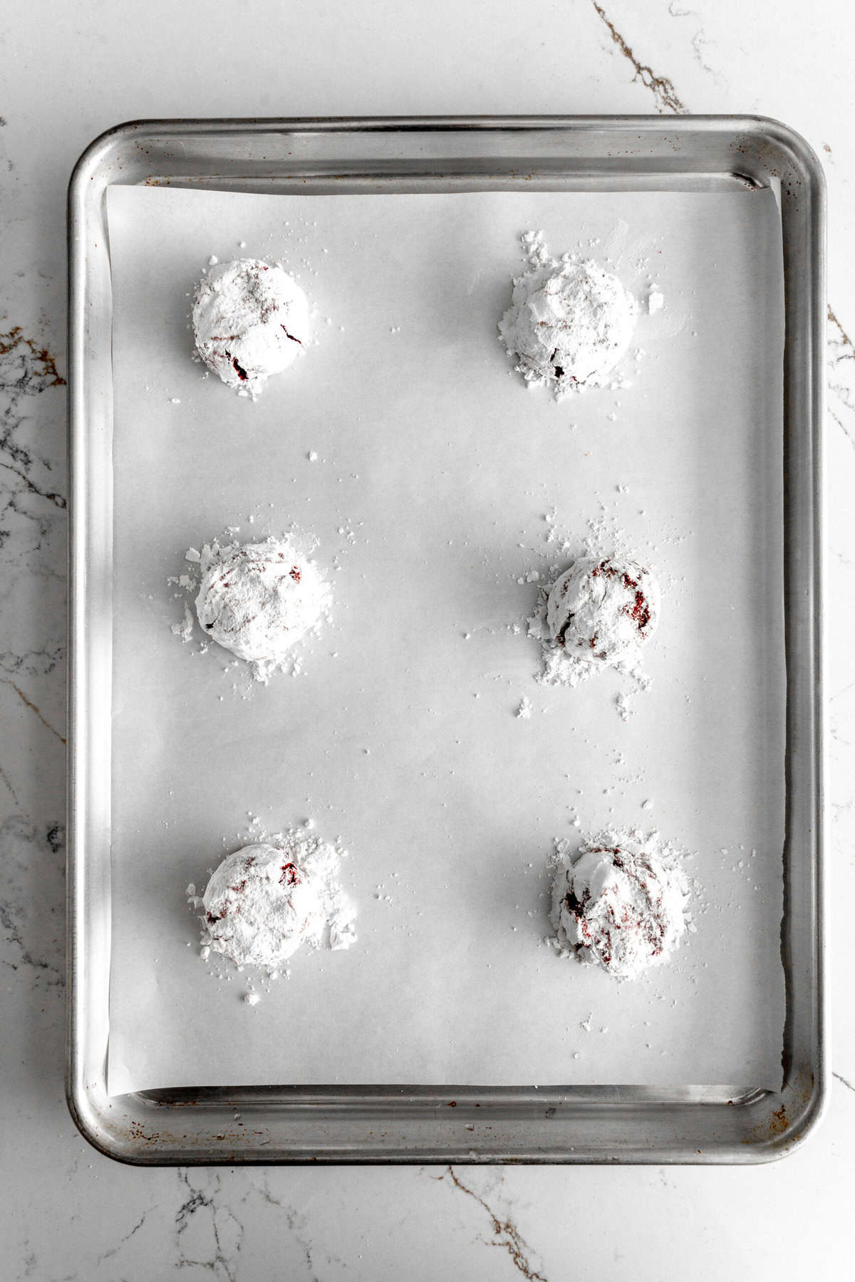 Unbaked red velvet crinkle cookies on a baking sheet.