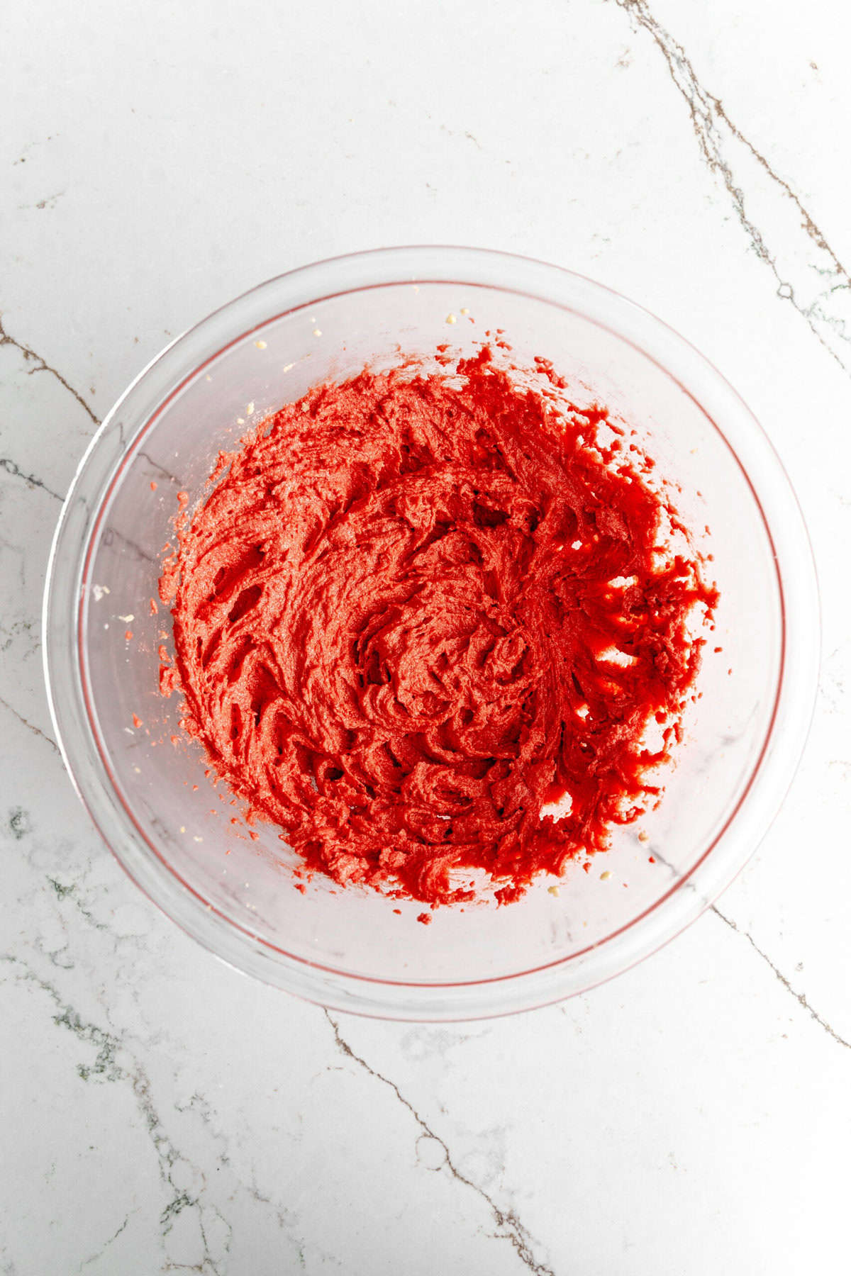 Creamed butter and sugar with red food coloring in a glass bowl.