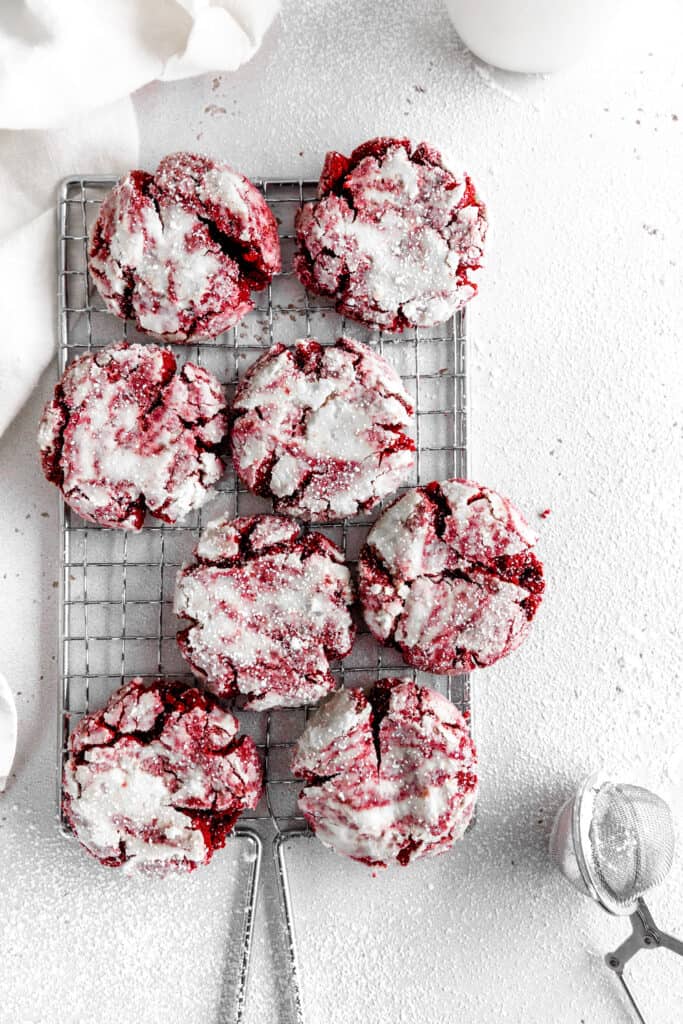 Red velvet crinkle cookies on a wire cooling rack, a linen napkin and a jug of milk.