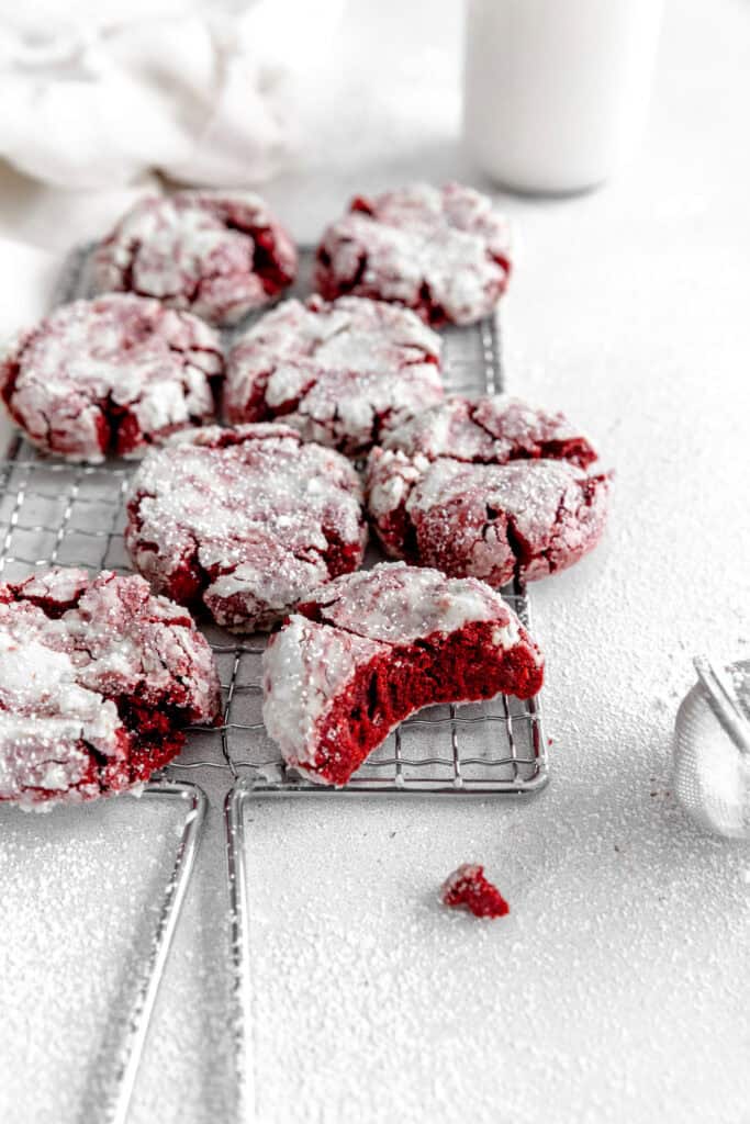 Red velvet crinkle cookie with a bite taken out of it on a wire cooling rack.