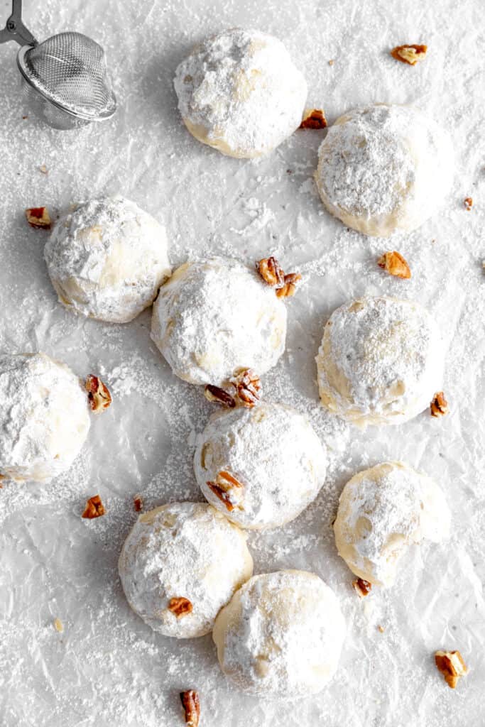 Snowball cookies on a white surface with chopped pecans.