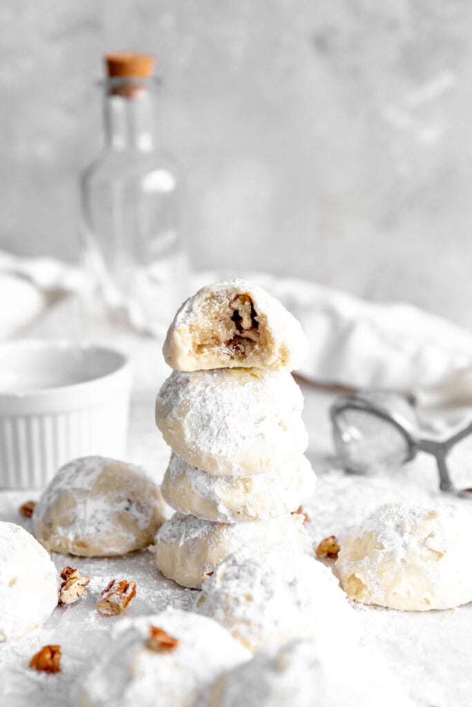 Stack of snowball cookies and a cup of powdered sugar.