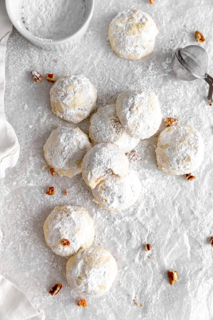 Snowball cookies on a white surface and a cup of powdered sugar.