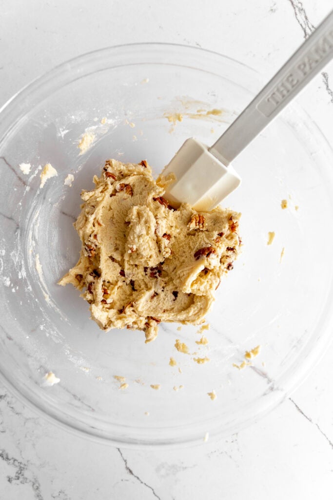 Snowball cookie dough in a glass bowl with a rubber spatula.