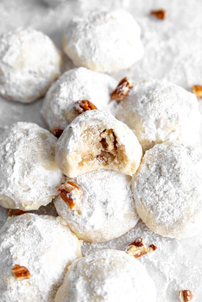 Snowball cookie with a bite taken out of it in a pile of more cookies.