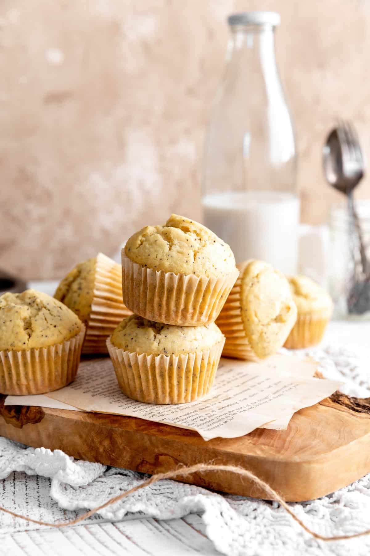 Pile of almond poppy seed muffins on a cutting board and a jug of milk.