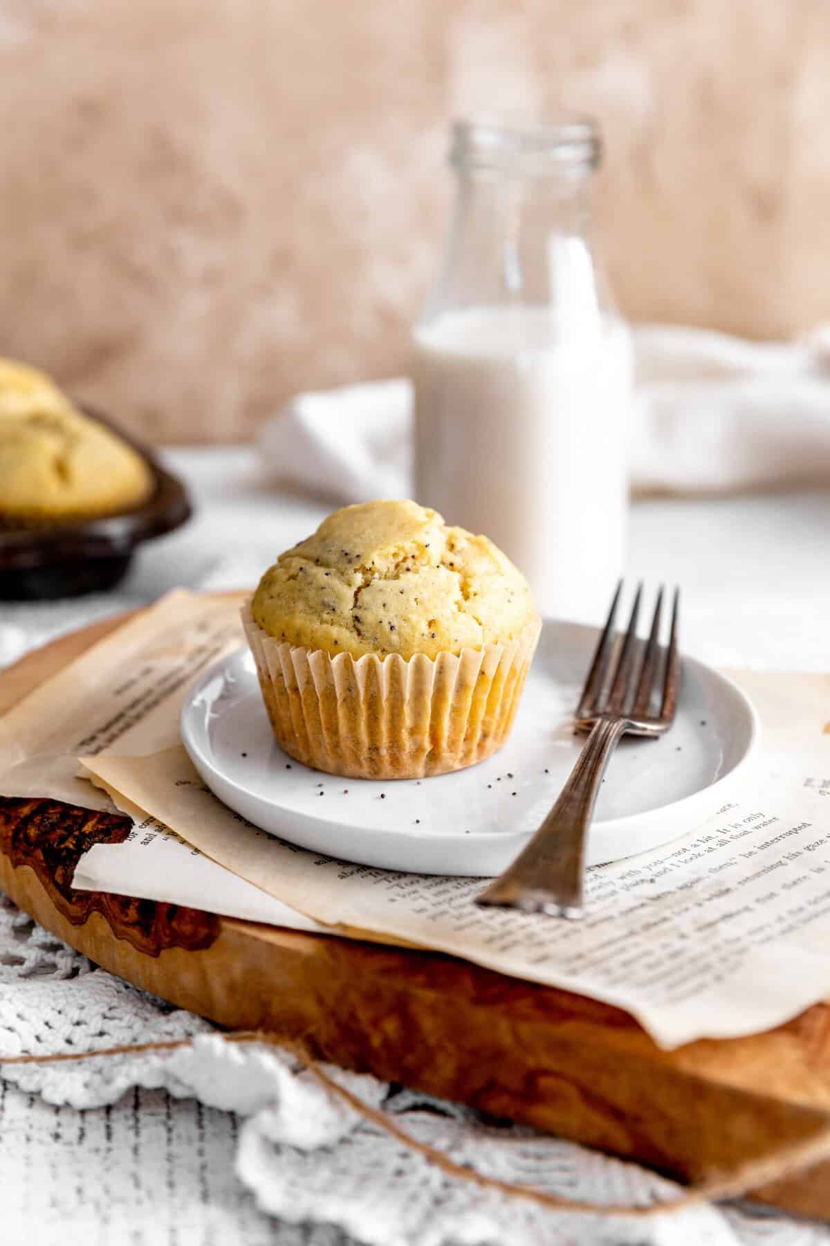 Almond poppy seed muffin on a plate with a fork and a jug of milk.