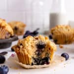 Blueberry muffin with a bite taken out of it and a jug of milk.