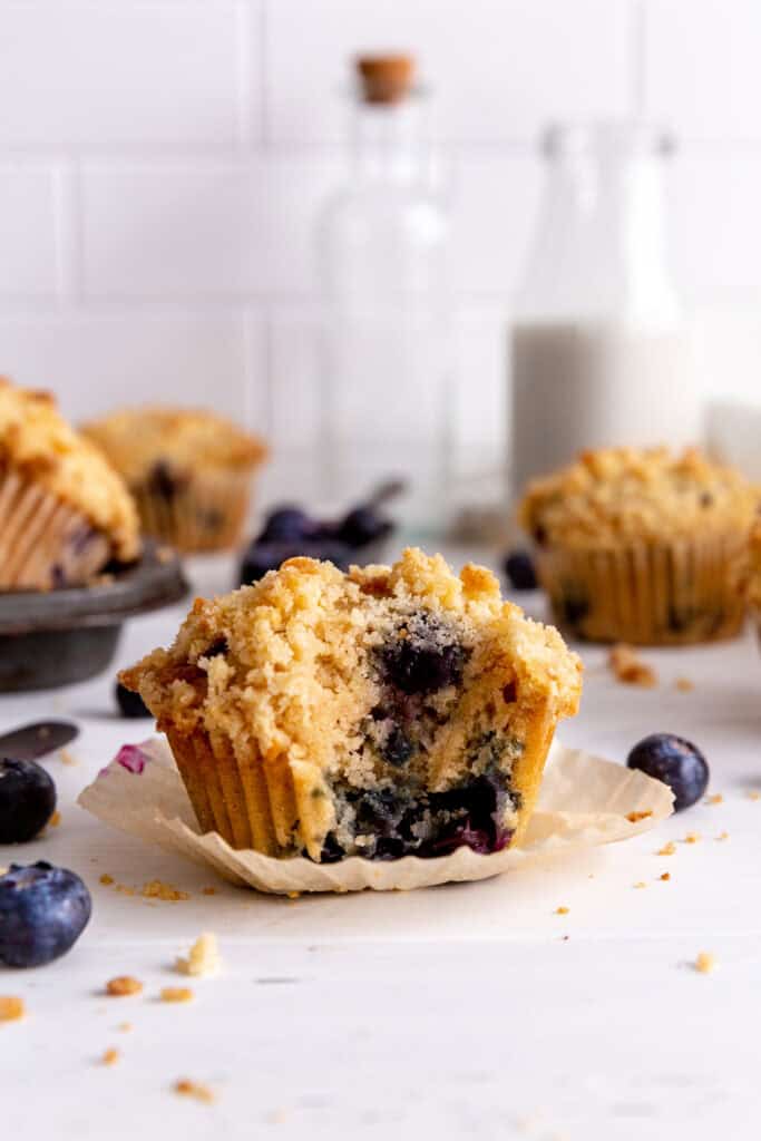 Blueberry muffin with a bite taken out of it and a jug of milk.