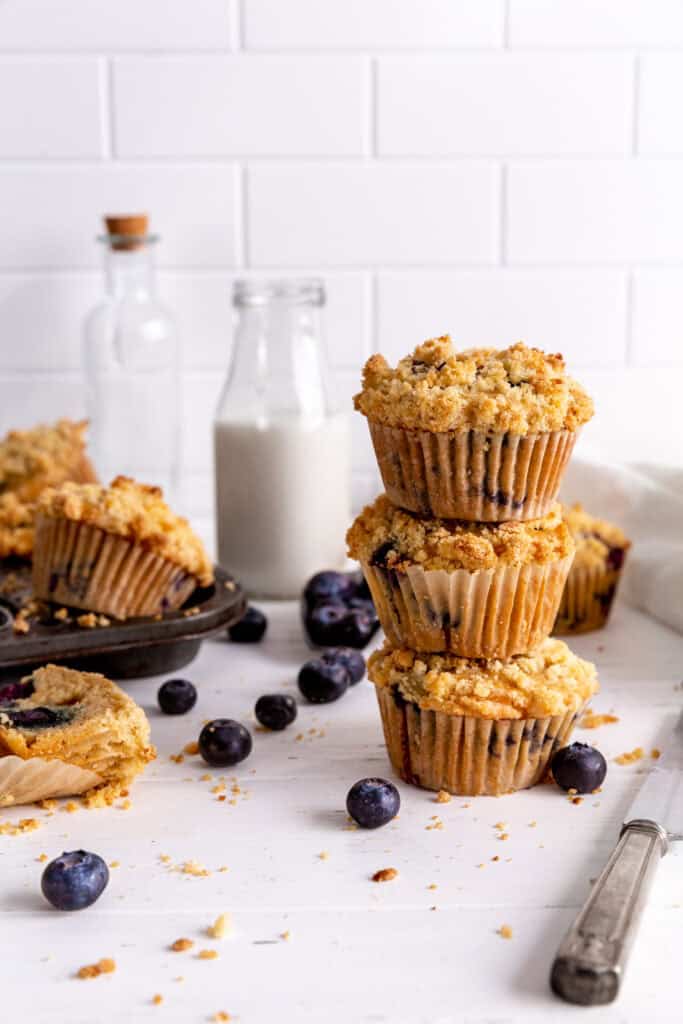 Stack of three blueberry muffins next to a pan of more muffins.