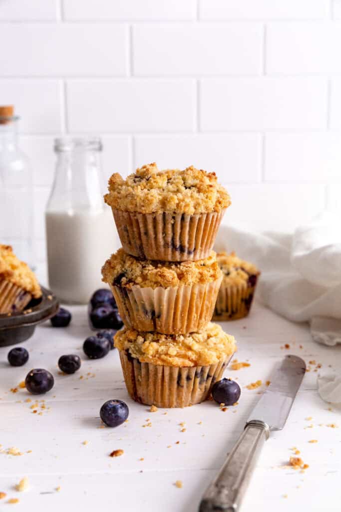 Stack of three blueberry muffins and a jug of milk.