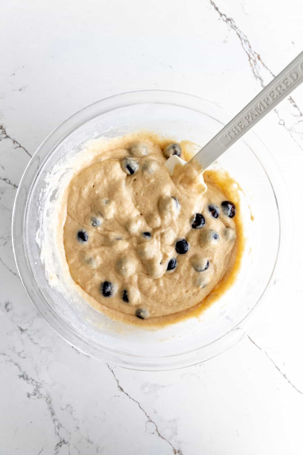 Glass bowl of blueberry muffin batter and a rubber spatula.