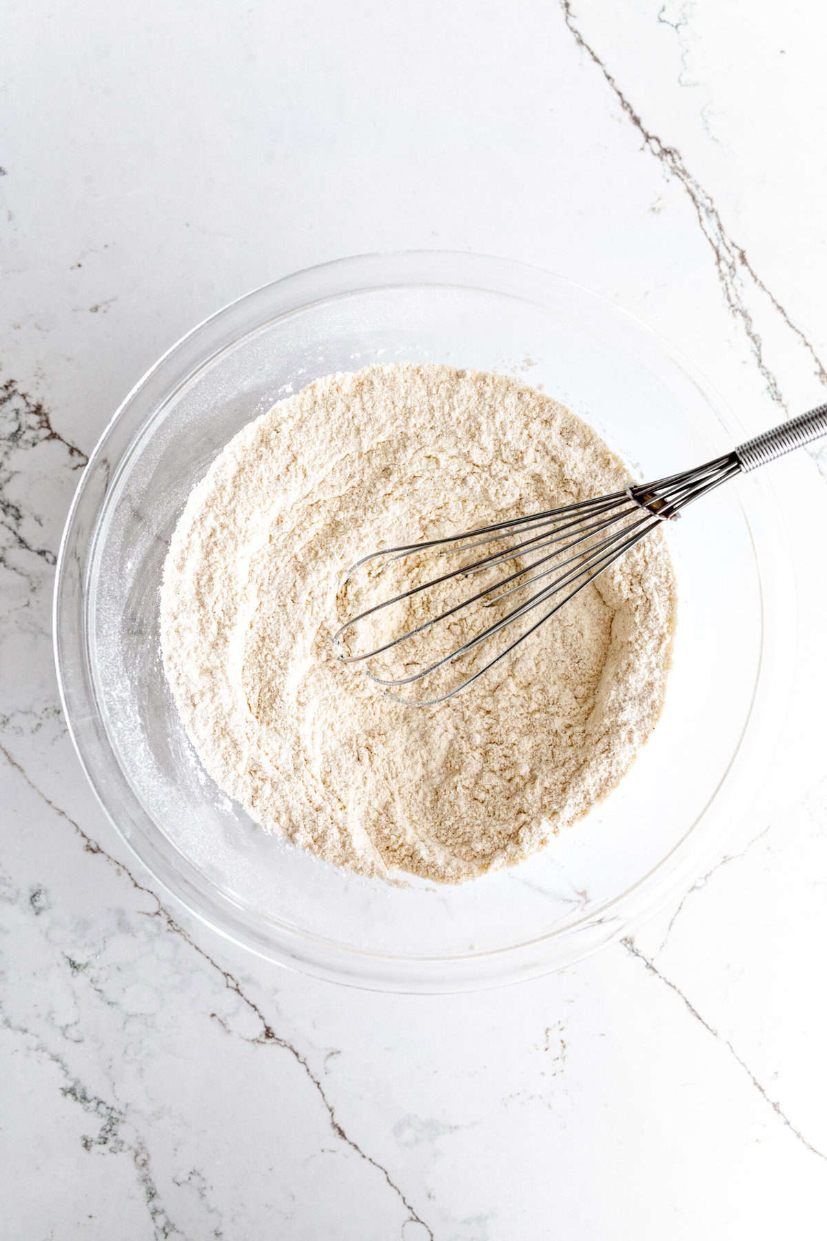 Glass bowl of flour and sugar with a whisk.