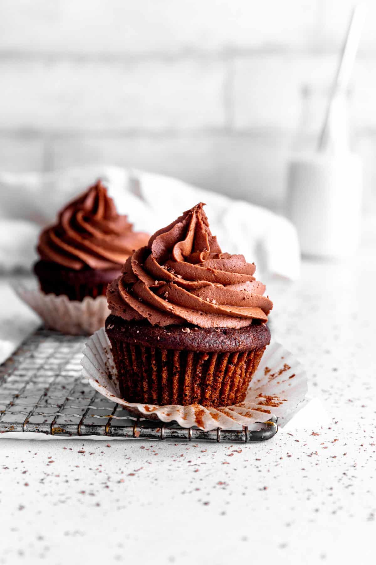 Unwrapped chocolate cupcakes on a wire cooling rack and a jug of milk.