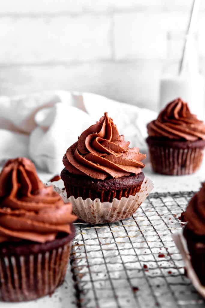 Unwrapped chocolate cupcake surrounded by more cupcakes and a linen napkin.