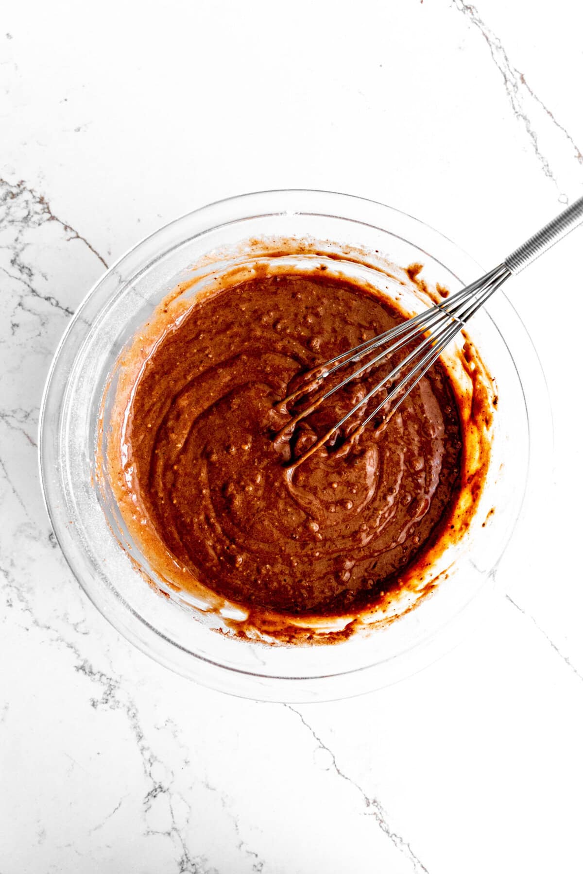 Glass bowl of chocolate cake batter and a whisk.