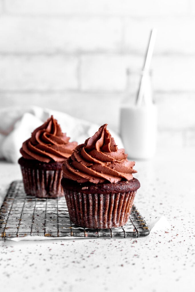 Chocolate cupcakes on a wire cooling rack in front of a jug of milk.