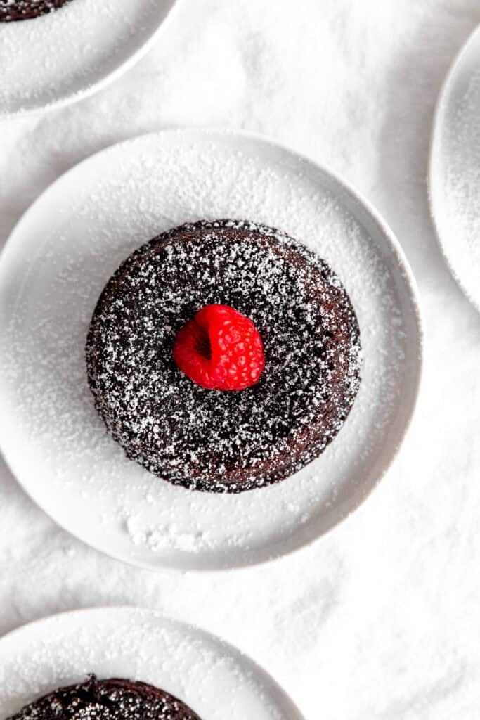 Chocolate lava cake topped with a raspberry on a white plate.