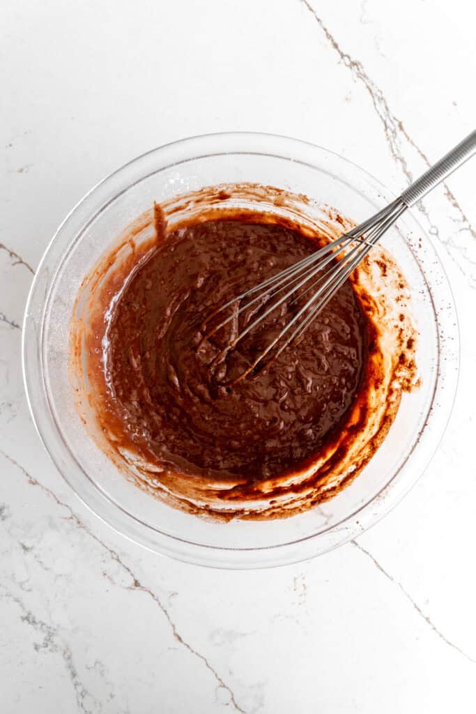 Glass bowl filled with chocolate cake batter and a whisk.