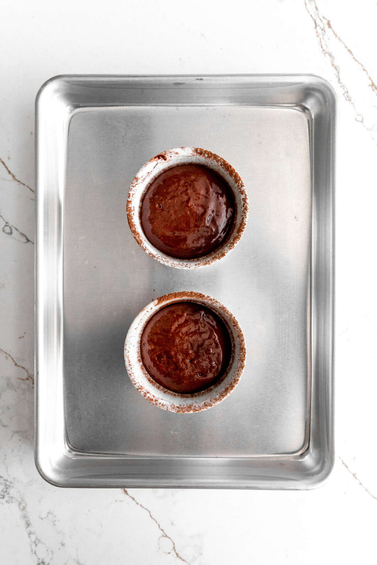 Unbaked chocolate lava cakes in ramekins on a baking sheet.