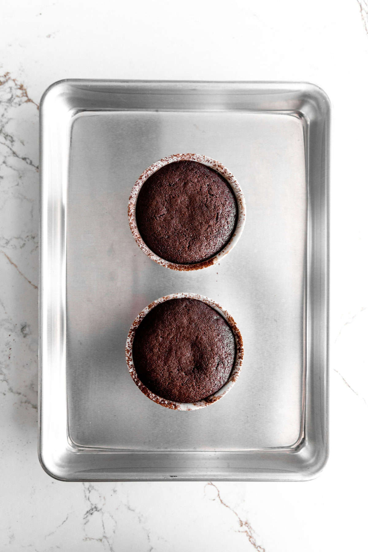 Baked chocolate lava cakes in ramekins on a baking sheet.