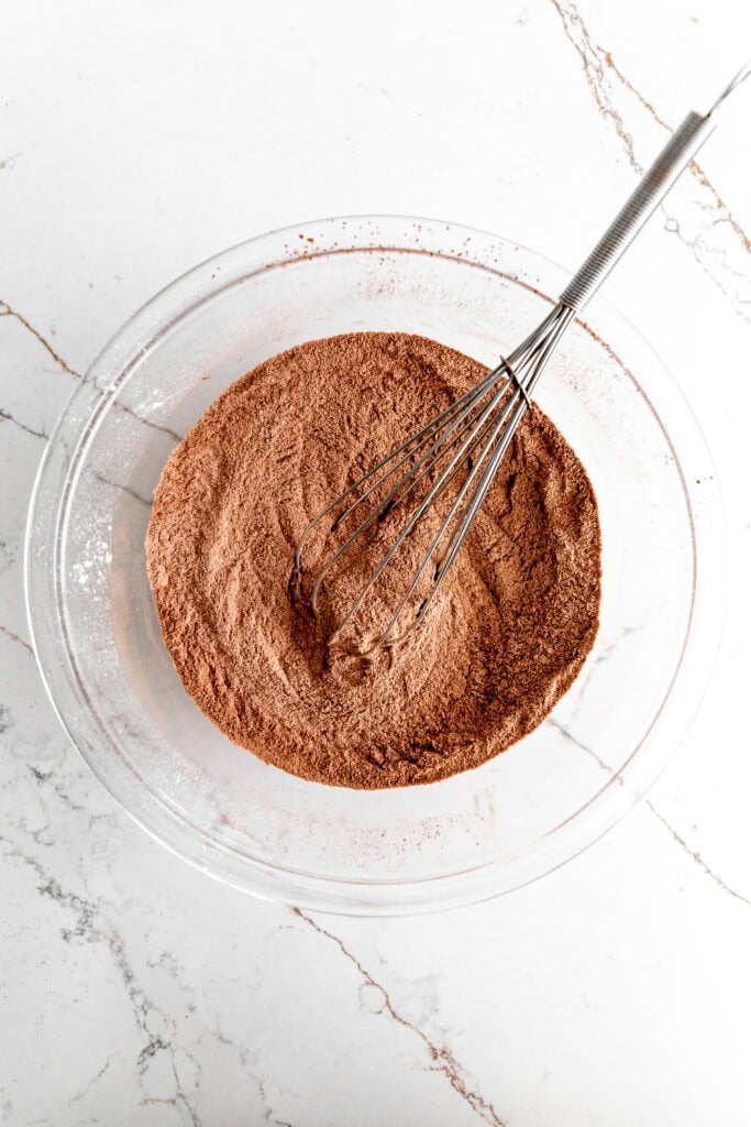 Glass bowl filled with dry chocolate cake ingredients and a whisk.