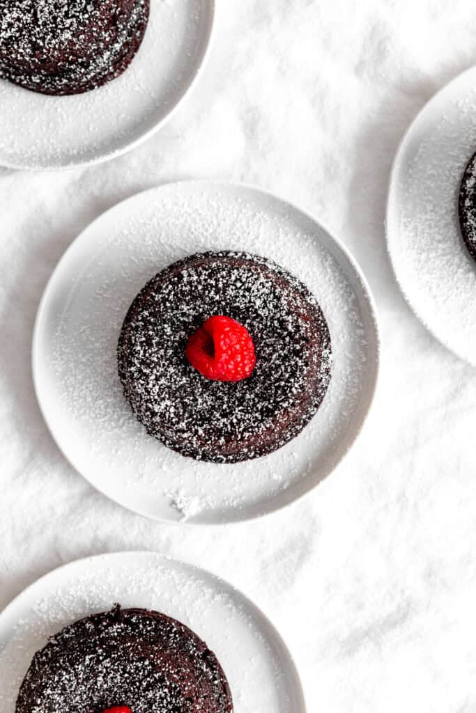 Chocolate lava cakes topped with a raspberries on white plates.