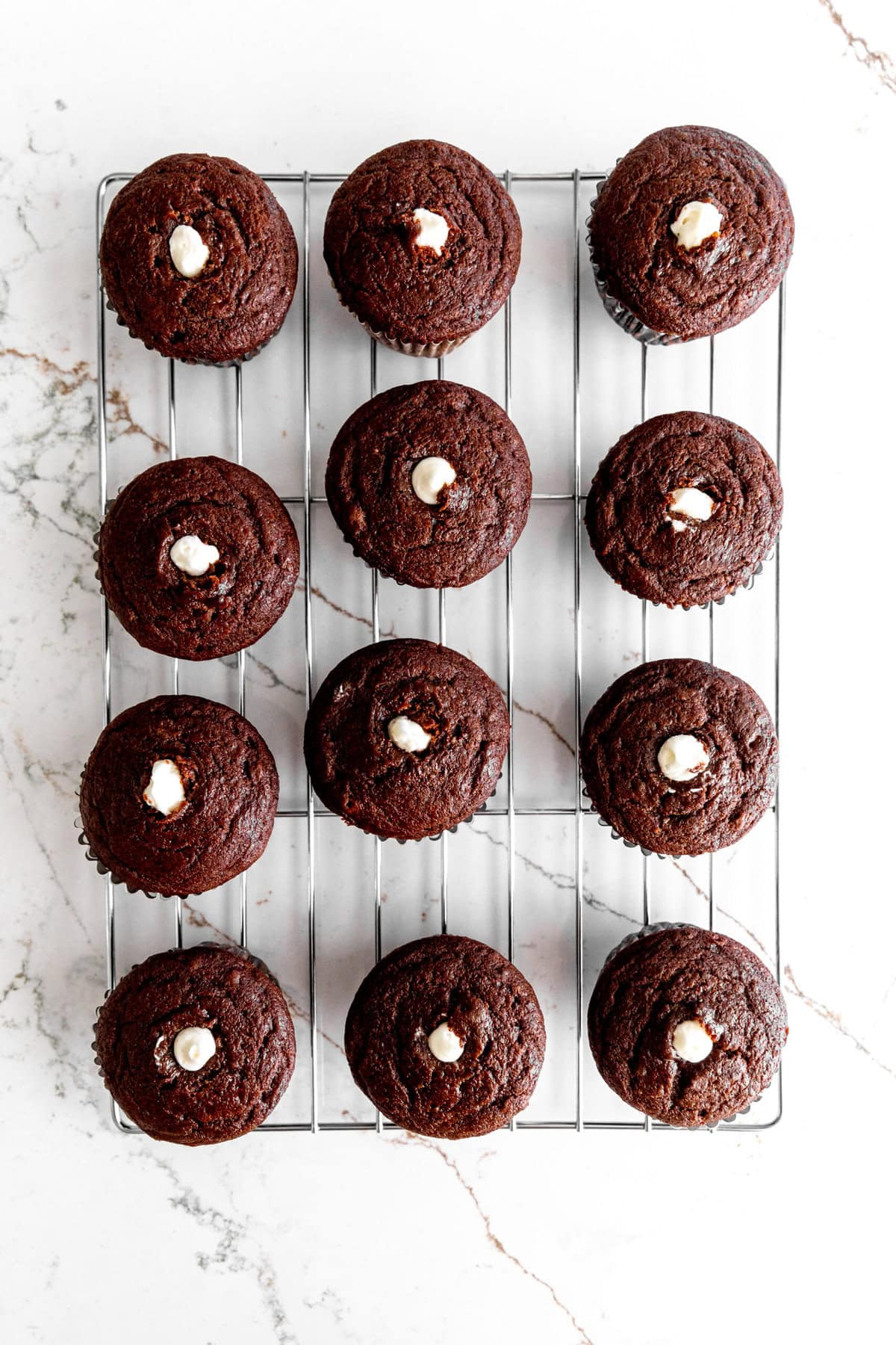 Chocolate cupcakes on a wire cooling rack filled with vanilla creme.