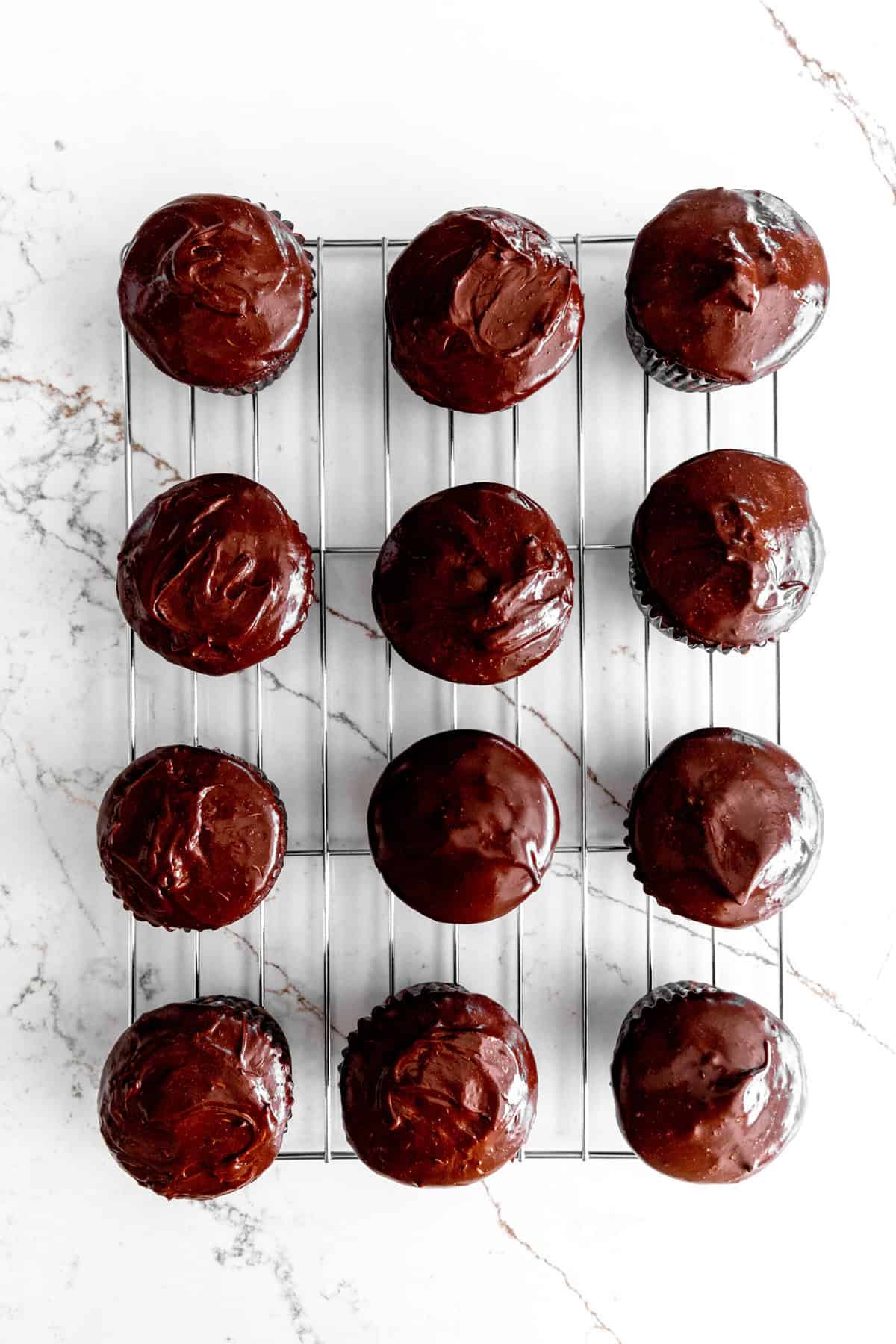 Chocolate cupcakes on a wire cooling rack topped with chocolate ganache.