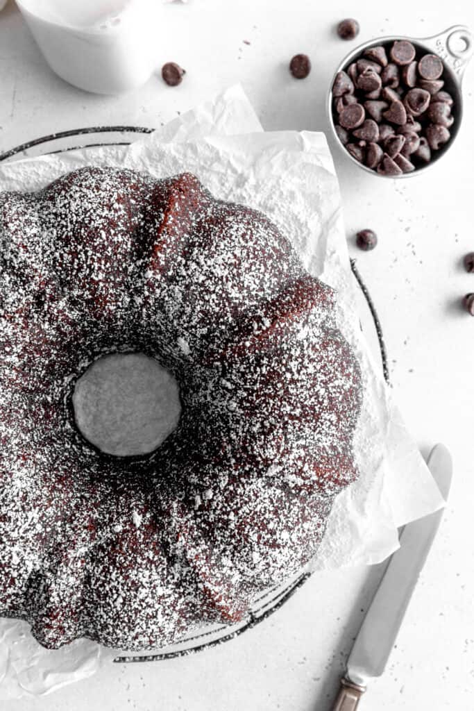 Kahlúa cake on a circular cooling rack, a jug of milk and a cup of chocolate chips.