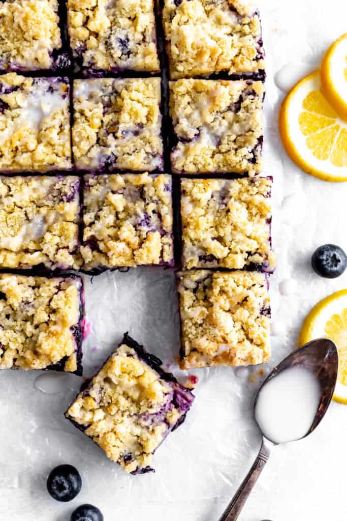 Lemon blueberry bars, a cup of blueberries, lemon slices and a spoon covered in glaze.